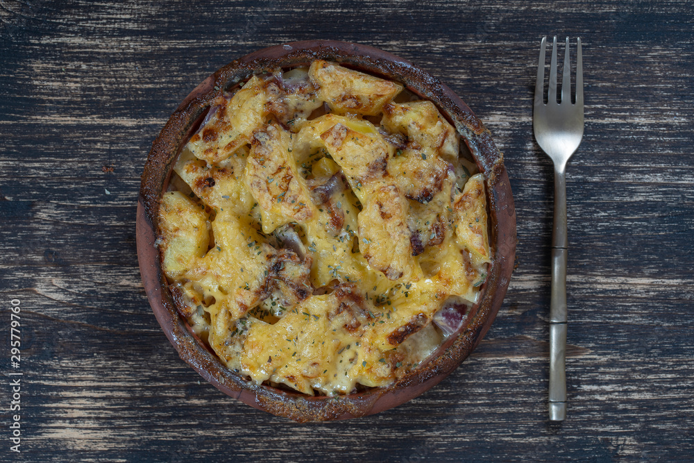 Baked potato, onion and garlic with cheese on the wooden table, close up. Ceramic bowl with potato onion and garlic slices background Baked potato, onion and garlic with cheese on the wooden table, close up. Ceramic bowl with potato onion and garlic slices background