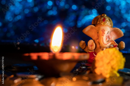 A beautiful, small Ganesha statue with a glowing lamp and a marigold flower in the foreground in Ganesh Chaturthi and Diwali-concept