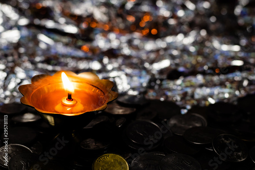 Top view of a glowing metal-lamp on a pile of coins and reflective background. Dhanteras concept