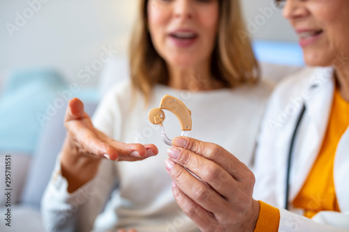 The doctor laryngologist explains senior woman how to wear a hearing aid. Mature female doctor hearing specialist in her office Showing Hearing Aid To female Patient In Clinic