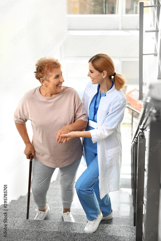 Fototapeta premium Nurse assisting elderly woman on stairs indoors