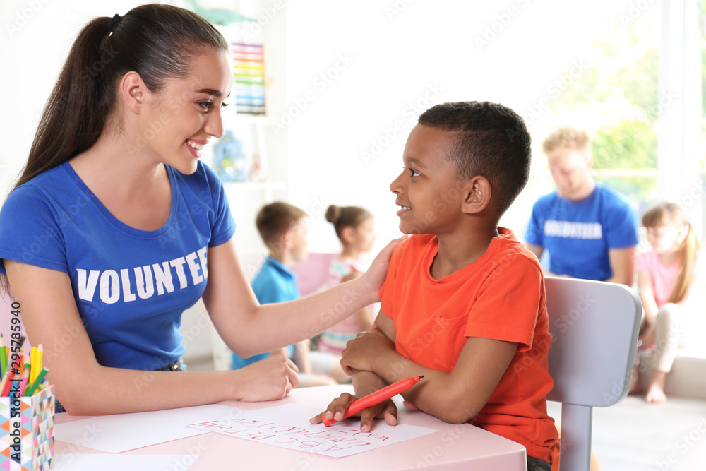 Little African-American boy learning alphabet with volunteer at table indoors Little African-American boy learning alphabet with volunteer at table indoors