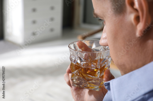 Young man with glass of whiskey at home. Space for text