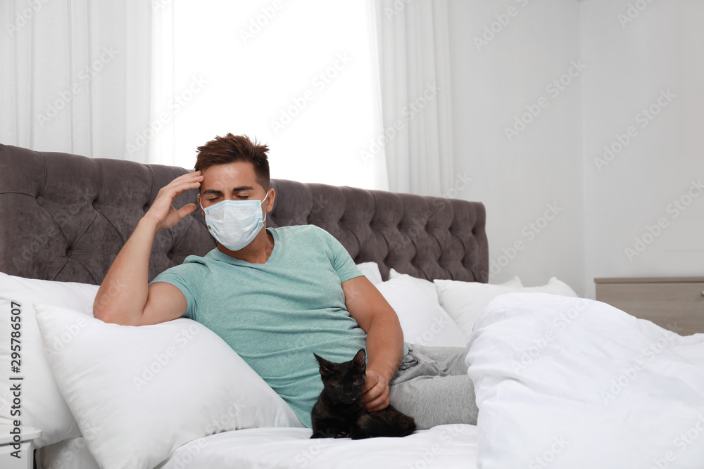 Young man with cat suffering from allergy in bedroom