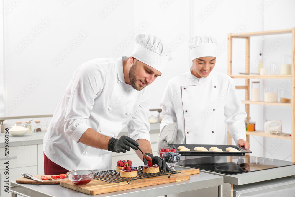 Pastry chefs preparing desserts at table in kitchen Pastry chefs preparing desserts at table in kitchen