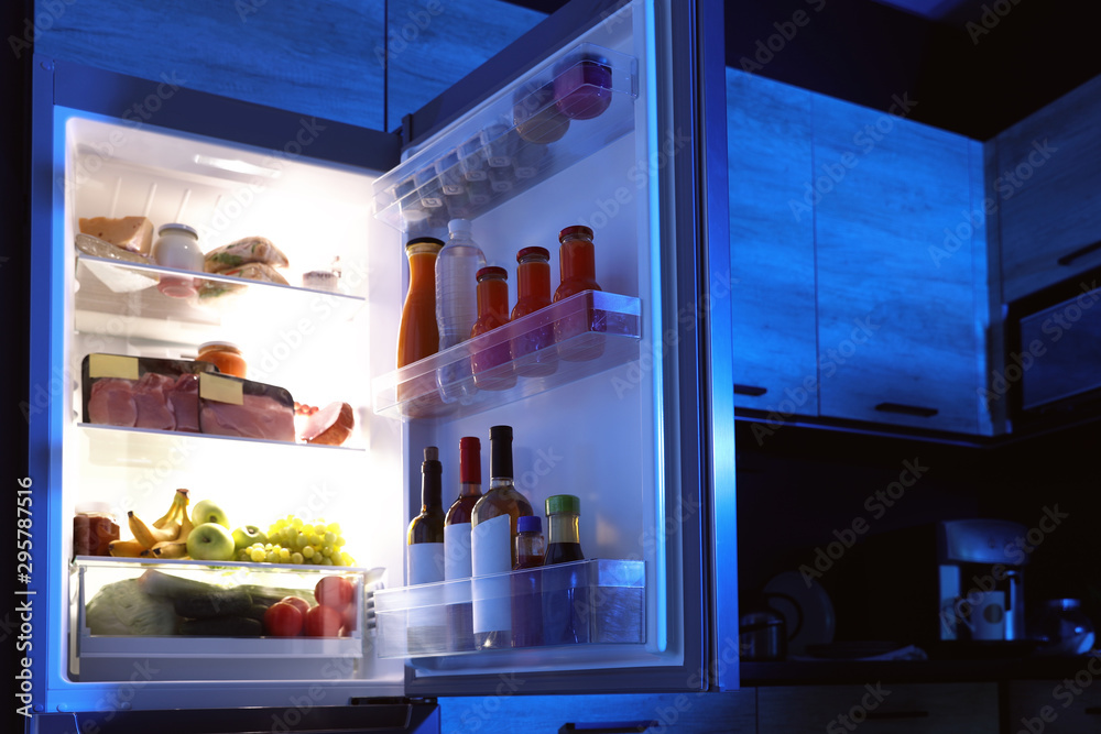 Open refrigerator full of products in kitchen at night