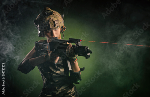 the girl in military airsoft clothes poses with a gun in her hands on a dark background © rotozey