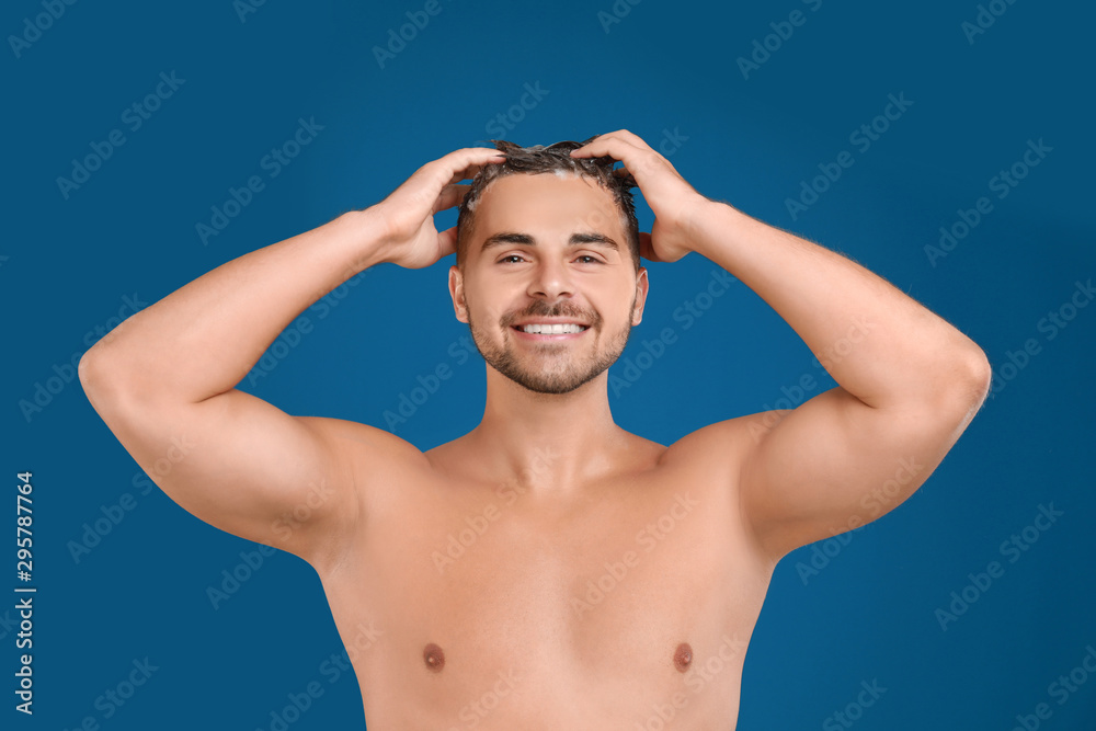 Fototapeta premium Young man washing hair on blue background