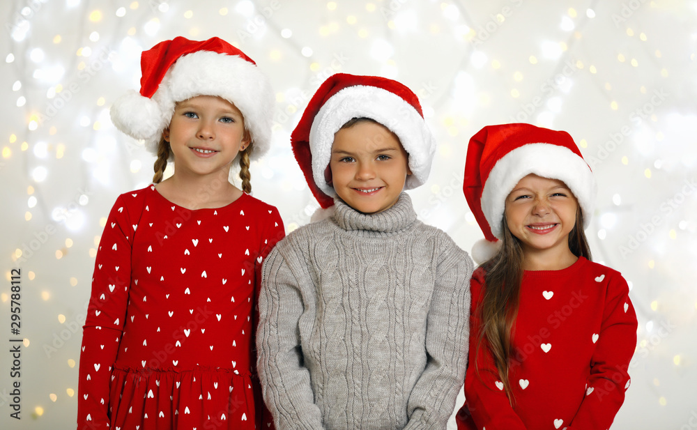 Happy little children in Santa hats against blurred festive lights. Christmas celebration Happy little children in Santa hats against blurred festive lights. Christmas celebration