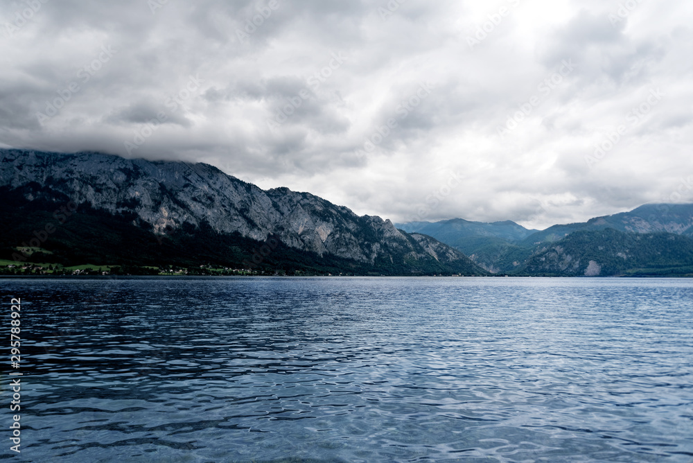 A cloudy day at Attersee lake at Salzkammergut area in Austria. There are a lot of green trees in the Alps mountains. The sky is full of grey clouds.