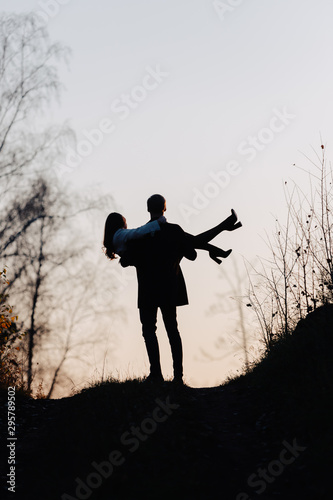 Silhouette of a man who holds a girl in his arms. Back view.