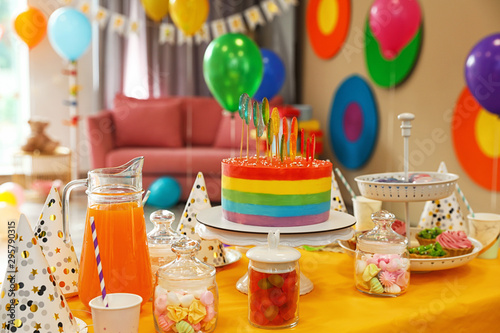 Bright birthday cake and other treats on table in decorated room