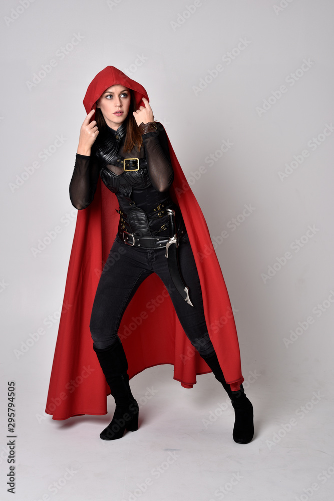 full length portrait of a pretty brunette woman wearing black leather fantasy costume with long red superhero cape. standing pose on a studio background. full length portrait of a pretty brunette woman wearing black leather fantasy costume with long red superhero cape. standing pose on a studio background.