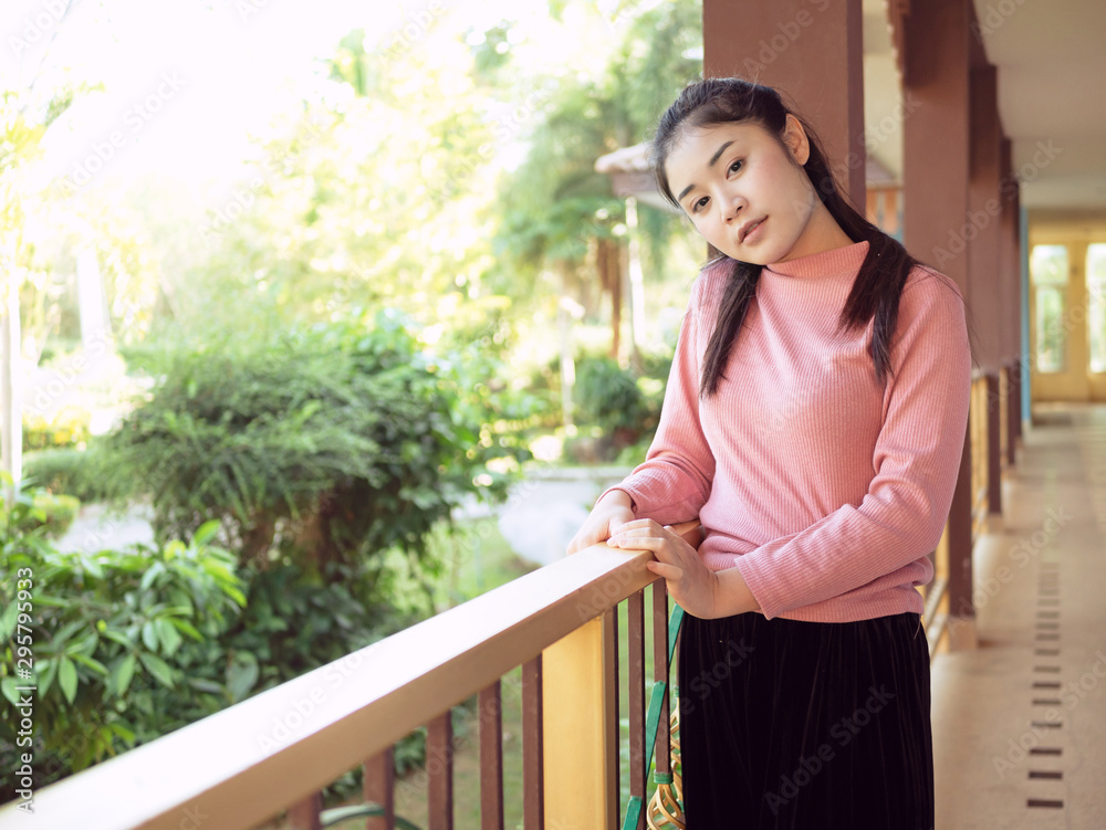 Asian teenage girls 25-30s, she had a beautiful and cute face, In a pink sweater and black pants. Standing on the balcony of the Resort or house with a garden in front.