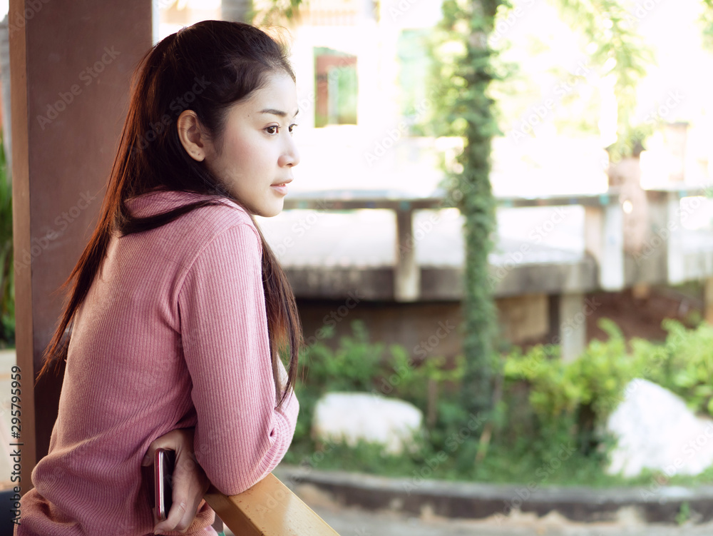 Asian teenage girls 25-30s, she had a beautiful and cute face, In a pink sweater and black pants. Standing on the balcony of the Resort or house with a garden in front.