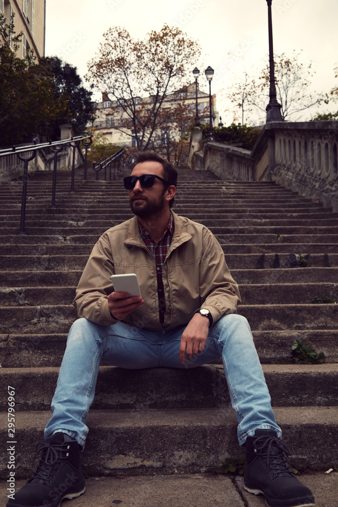 Obraz premium Handsome man sitting on stairs and using cellphone.