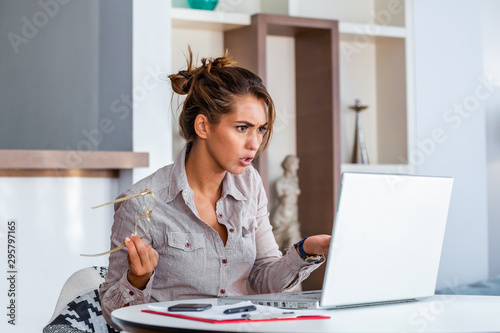 Young businesswoman misunderstanding her laptop at her desk in office. woman working with laptop at home or modern office. Serious, confused, or frustrated expression. photo