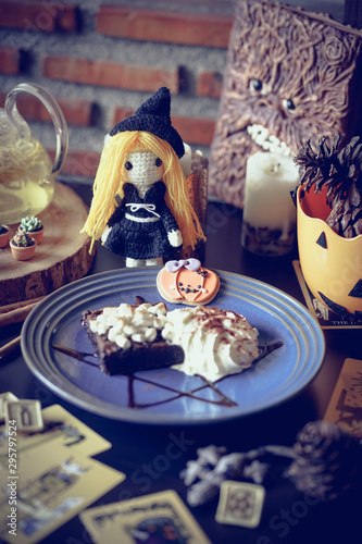 Halloween cafe and witchcraft party with herbal afternoon tea and macaron dessert in wicca and pegan concept with tarot cards. Selective focus on the cute crochet witch doll. Vignette and dark filter.