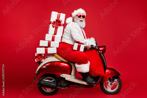 Profile side view of nice bearded cheerful fat funky Santa riding moped carrying pile stack fairy purchases shopping discount isolated on bright vivid shine vibrant red color background