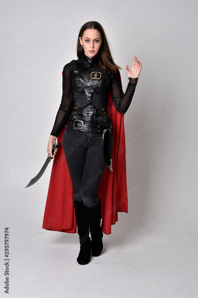 full length portrait of a pretty brunette woman wearing black leather fantasy costume with long red superhero cape. standing pose on a studio background. full length portrait of a pretty brunette woman wearing black leather fantasy costume with long red superhero cape. standing pose on a studio background.