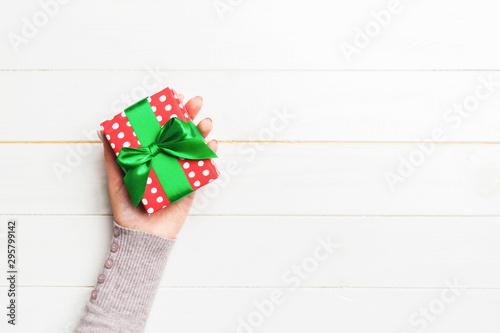 Girl Hands holding craft paper gift box with as a present for Christmas or other holiday on white wooden background, top view with copy sppace photo