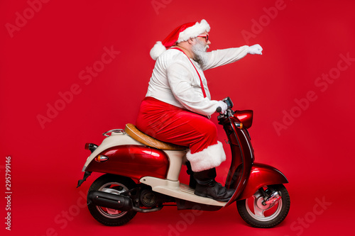 Profile side view portrait of nice bearded serious purposeful Santa Claus father riding moped delivering purchases hurry up shopping season isolated on bright vivid shine vibrant red color background