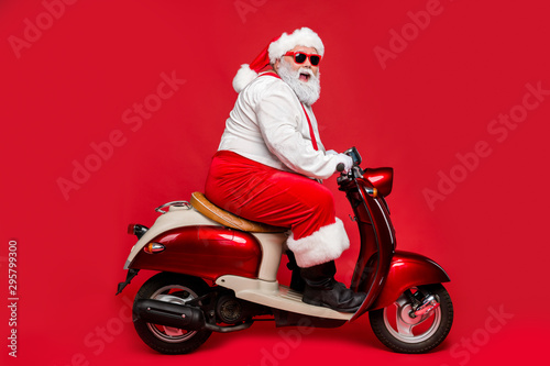 Profile side view portrait of nice bearded cheerful cheery funny Santa father riding motor bike having fun shopping winter season isolated on bright vivid shine vibrant red color background