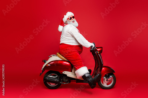 Profile side view portrait of nice bearded cheerful funny Santa St Nicholas father riding motor bike having fun wintertime christmastime isolated on bright vivid shine vibrant red color background