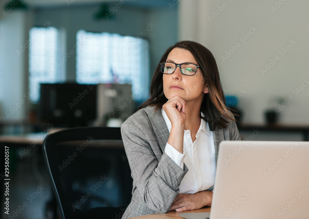 Businesswoman thinking about work while sitting at her office desk - obrazy, fototapety, plakaty 