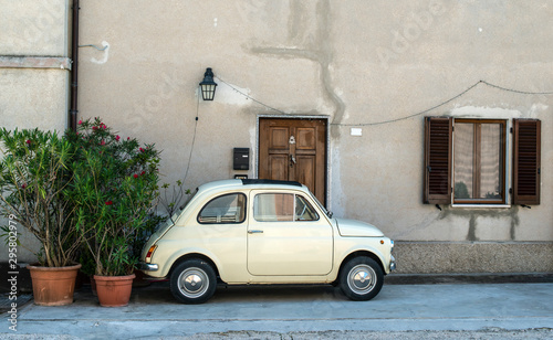 Fototapeta Naklejka Na Ścianę i Meble -  Small vintage italian car. Beige color old car in front of old house facade and flowers..