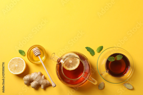 Flat lay. Cup of tea, teapot, lemon, ginger, mint, honey and dipper on yellow background, copy space