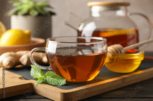 Cup of tea, mint, honey, ginger and teapot on wooden background, space for text