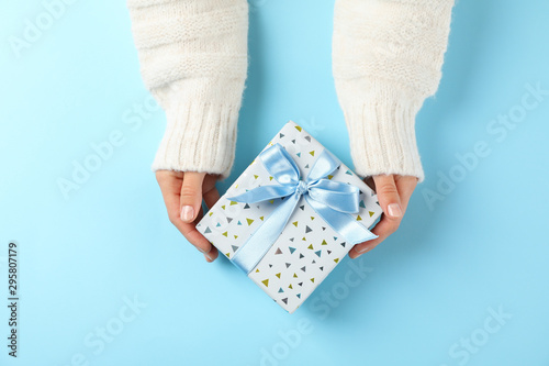 Young woman holding gift box on light blue background, space for text