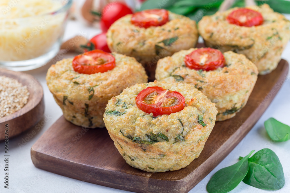 Savory muffins with quinoa, cheese and spinach topped with tomato, on  wooden board, horizontal