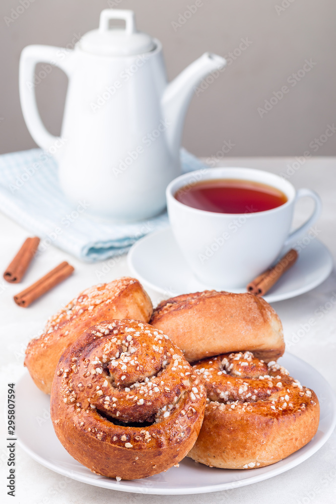 Cinnamon buns on  white plate, served with a cup of red tea, vertical