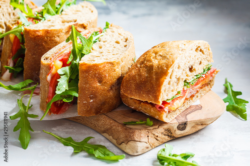 Sandwiches with ciabatta, cheese, ham and vegetables on a wooden board.