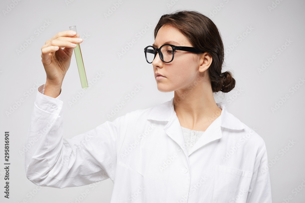 Portrait of pretty young woman wearing lab coat and holding test tube with blue liquid standing against white background, copy space Portrait of pretty young woman wearing lab coat and holding test tube with blue liquid standing against white background, copy space