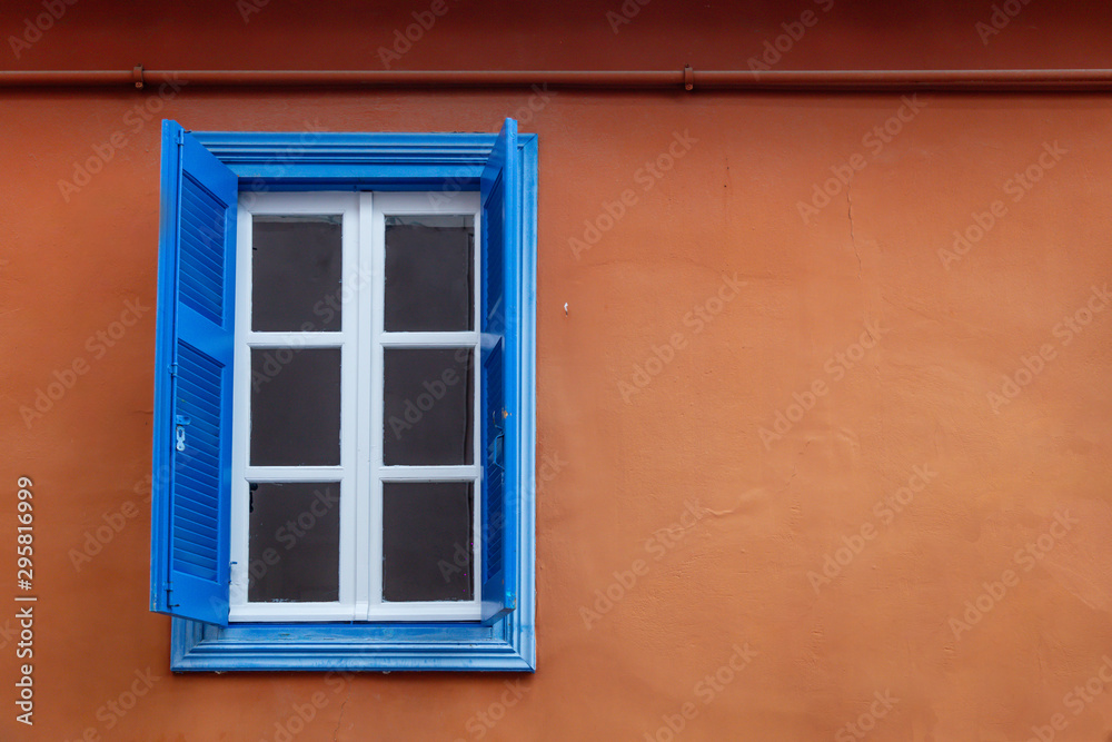 Window with blue wooden, open shutters on light brown wall. Facade of village building, copyspace, closeup.