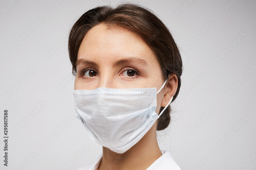 Head and shoulders portrait of female doctor wearing protective mask and looking at camera posing against white background Head and shoulders portrait of female doctor wearing protective mask and looking at camera posing against white background