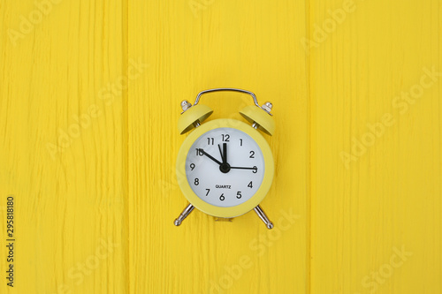 yellow old style alarm clock on yellow wooden background
