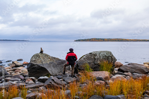 A young European man enjoys the view of the cold Northern lake. A lone traveler stands on a rocky shore