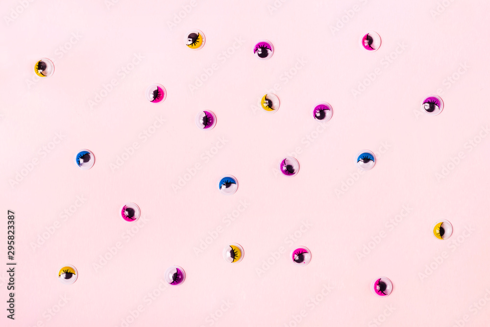 Pink pastel background with round toy eyes in different colors. Funny holiday flat lay concept