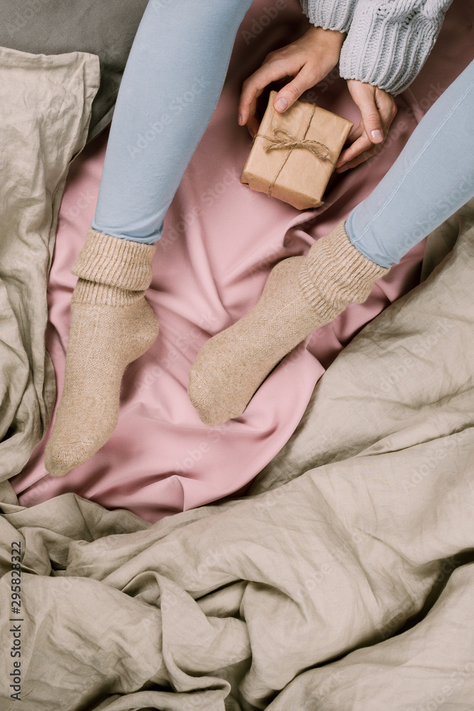 Cozy flatlay of woman's legs in blue leggins and warm socks holding gift box, selective focus