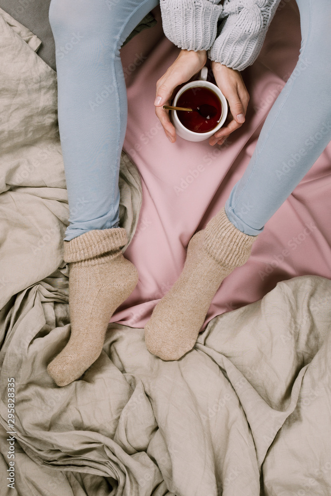 Cozy flatlay of woman's legs in blue leggins and warm grey socks in bed with cup of tea, selective focus Cozy flatlay of woman's legs in blue leggins and warm grey socks in bed with cup of tea, selective focus