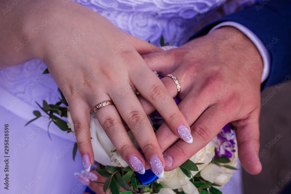 Fototapeta premium Hands of the bride and groom in wedding rings on a background of flowers.