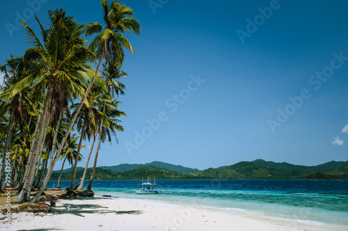 El Nido, Palawan, Philippines. Coconut palm trees on sandy beach and lonely filippino banca boat in turquoise ocean water. Island hopping tour with beautiful tropical scenery
