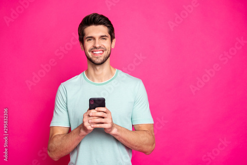 Photo of blogger guy holding telephone in hands checking subscribers toothy smiling wear casual outfit isolated vivid pink color background © deagreez