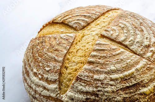 A close up of a freshly baked sourdough bread showing the traditional markings standing on a marble base