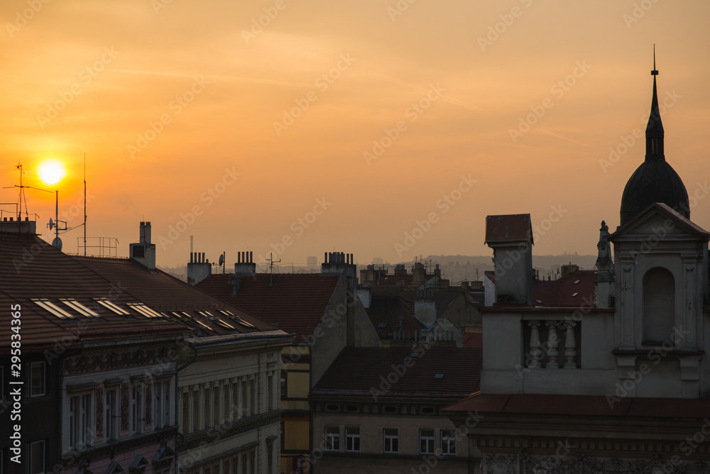 View of the roofs of historic buildings with red tiles during a bright sunset in Prague, Czech Republic.