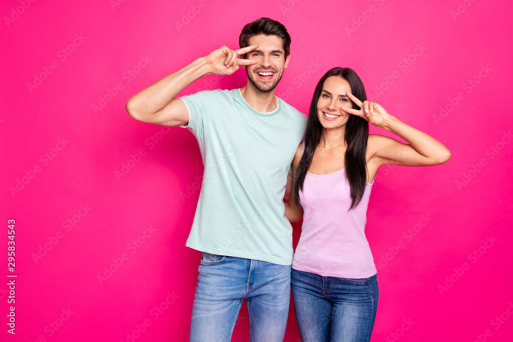Photo of funny couple guy and lady raising hands showing v-sign symbols near eyes wear casual clothes isolated bright pink color background Photo of funny couple guy and lady raising hands showing v-sign symbols near eyes wear casual clothes isolated bright pink color background